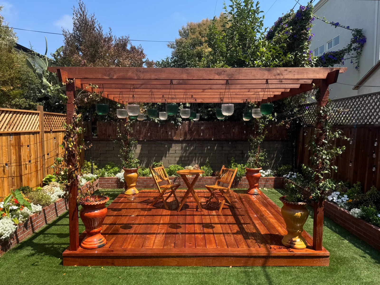 A wooden garden pergola with a table, chairs, and climbing plants