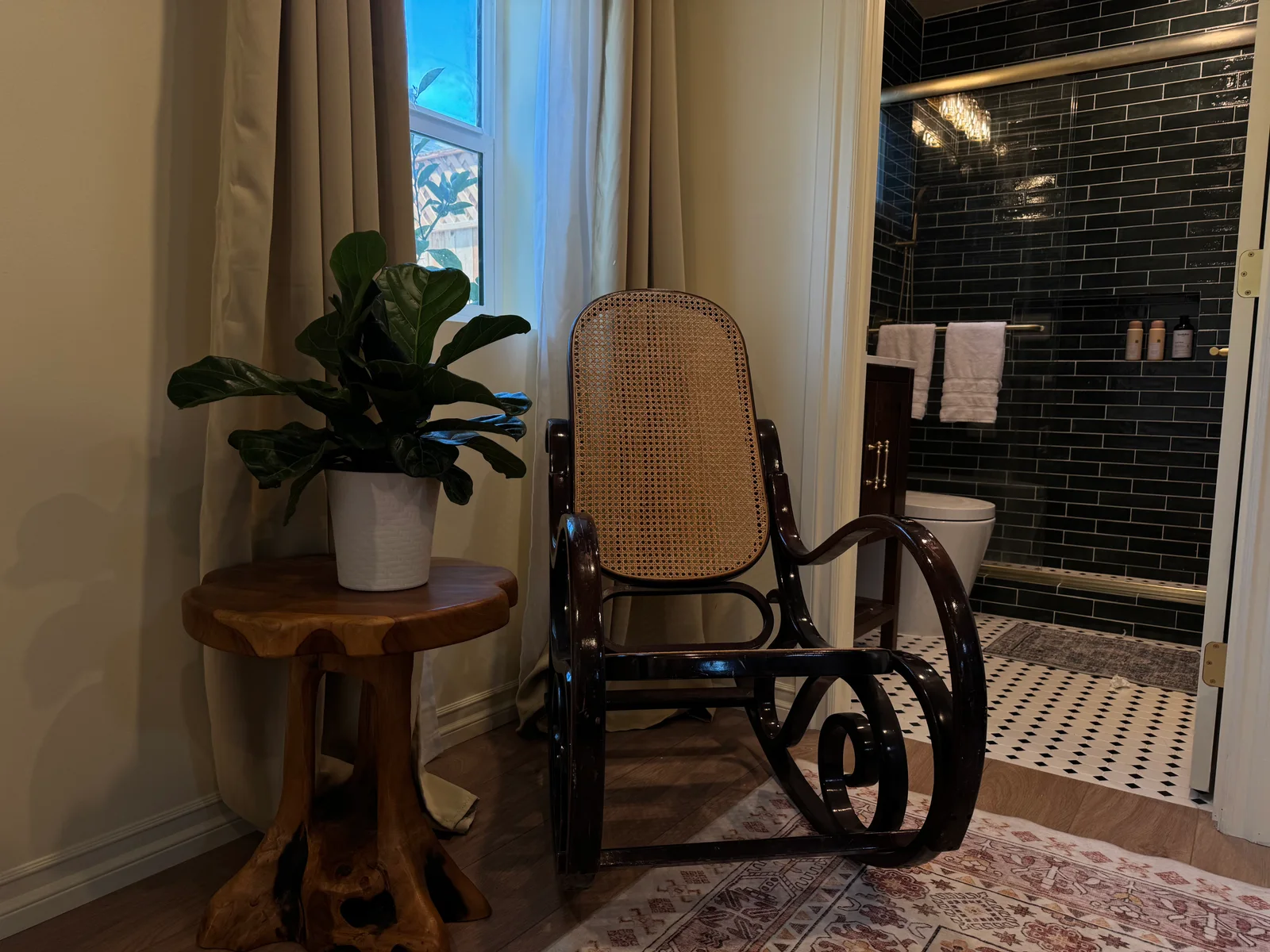 A cane rocking chair beside a plant and an open bathroom doorway